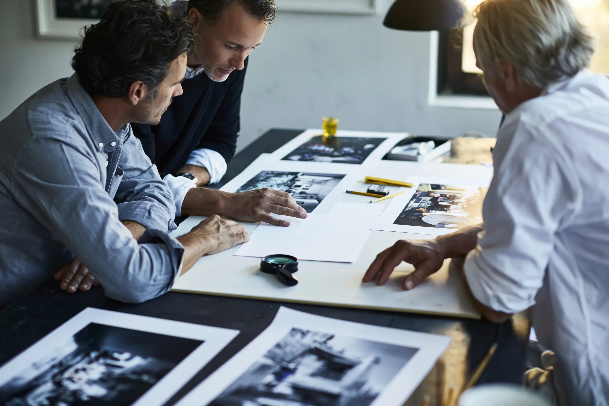 Three colleagues reviewing printed photographs laid out on a table